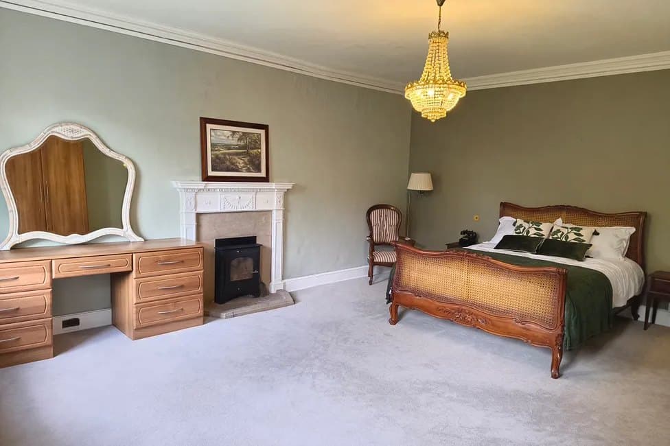 A bedroom with a carved sleigh bed, dressing table and white marble fireplace