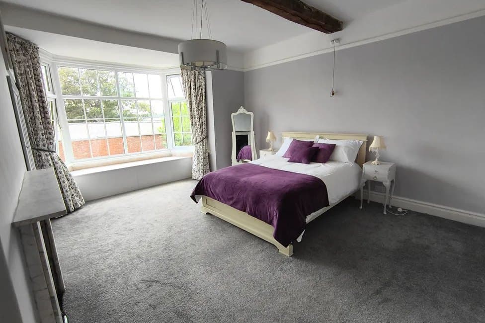 A bedroom in soft grey with a purple throw and a mirrored side table