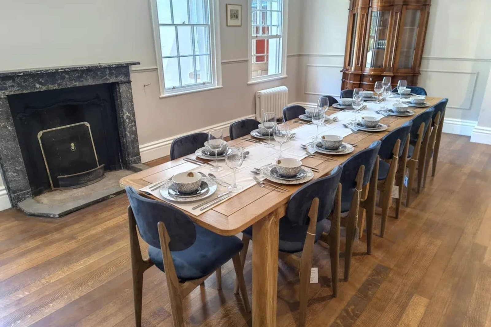 The formal dining room laid for twelve, with a long oak table, blue upholstered chairs and a marble fireplace