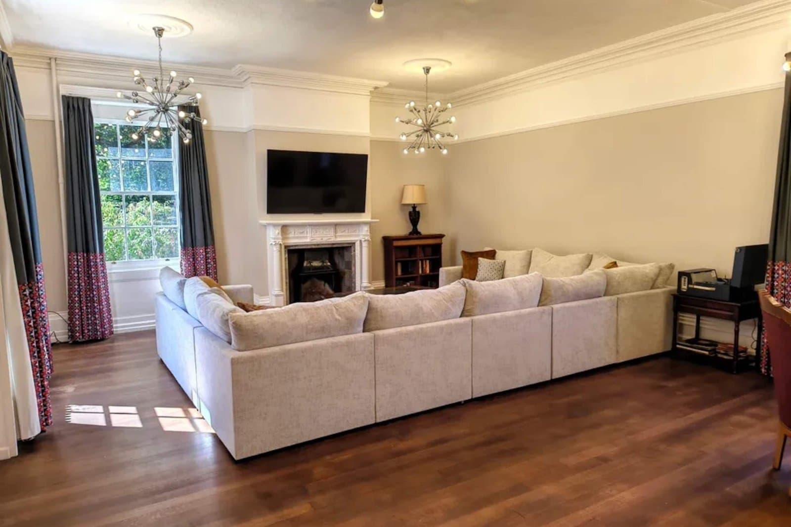 The main drawing room with deep cream sofas along one wall, an open fireplace and tall sash windows over polished wood floors