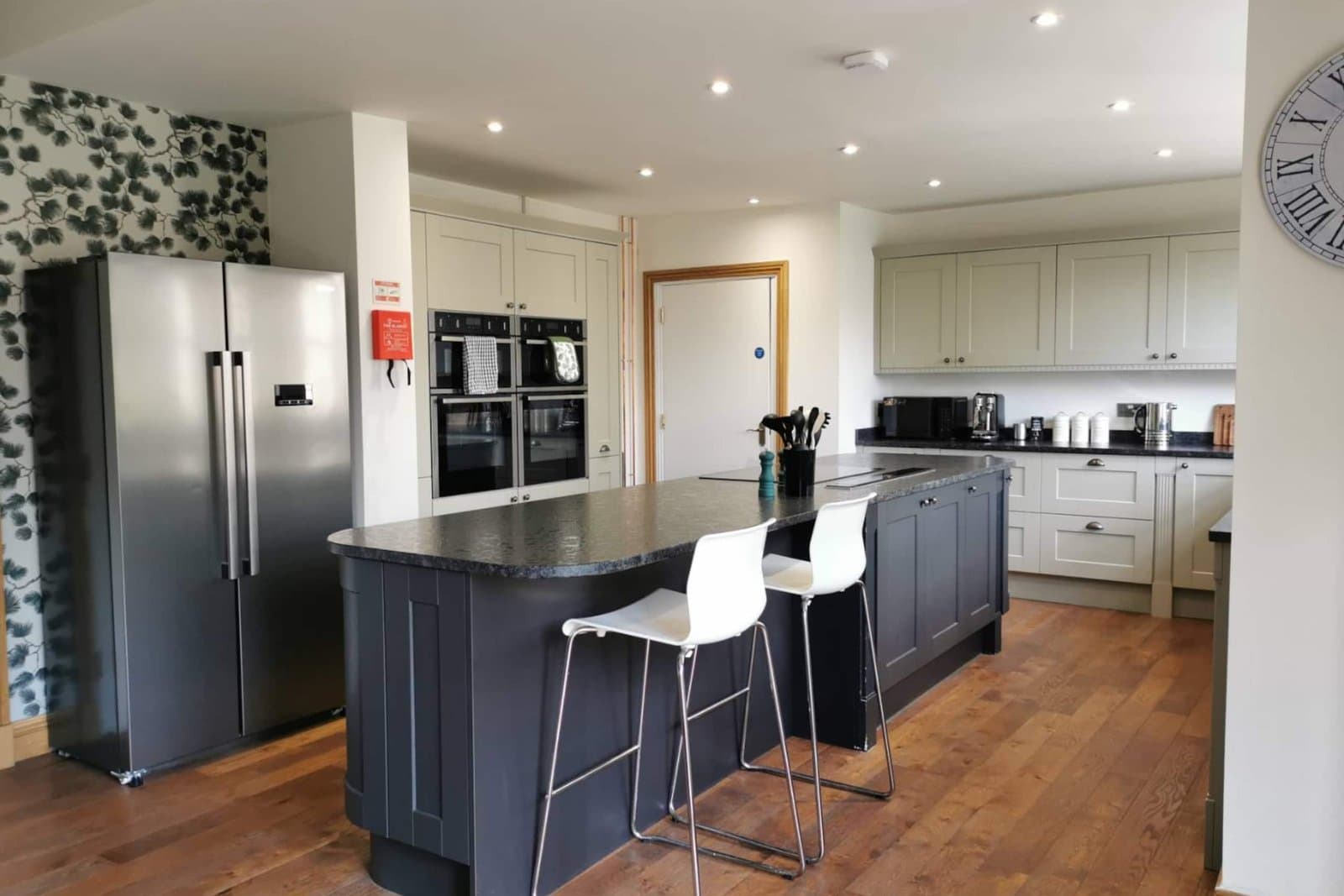 The kitchen with a navy island and breakfast-bar stools, American fridge freezer and double ovens