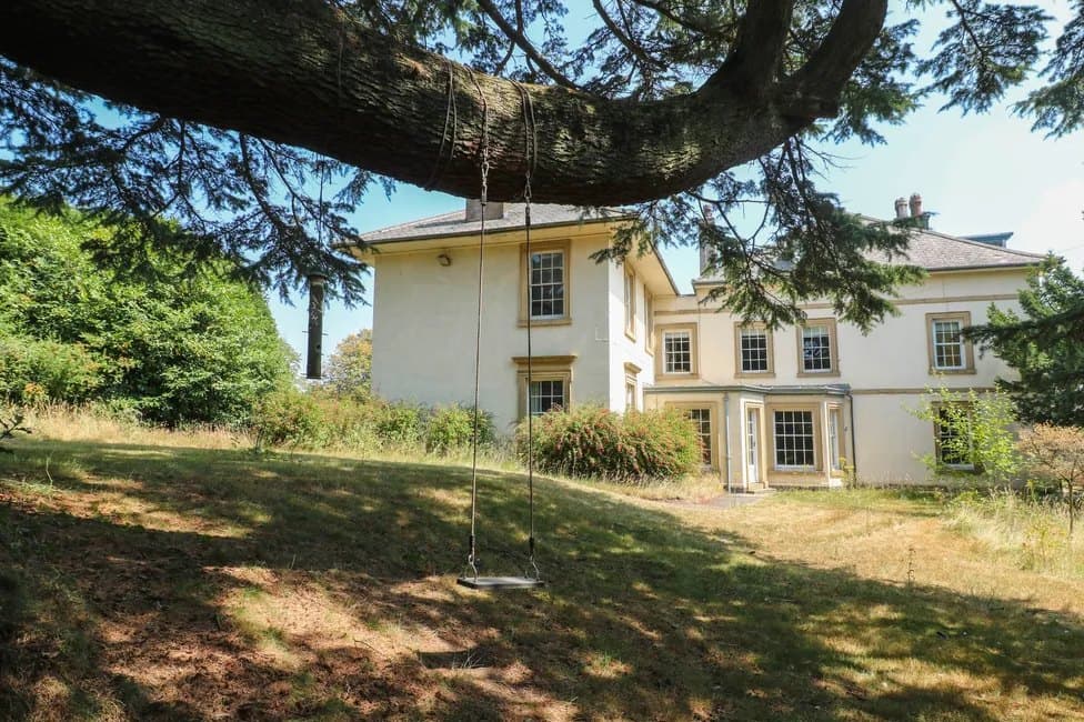 The manor in summer, seen across the lawn from beneath a cedar