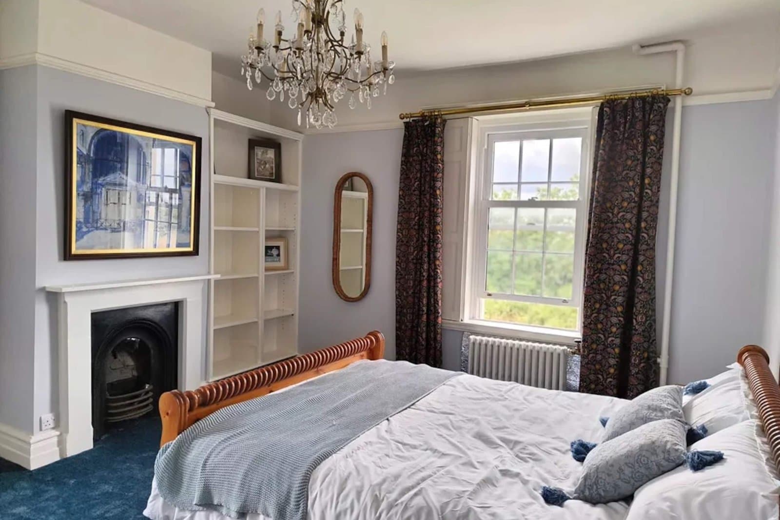 A bedroom with a wooden sleigh bed, cut-glass chandelier, cast-iron fireplace and deep blue carpet