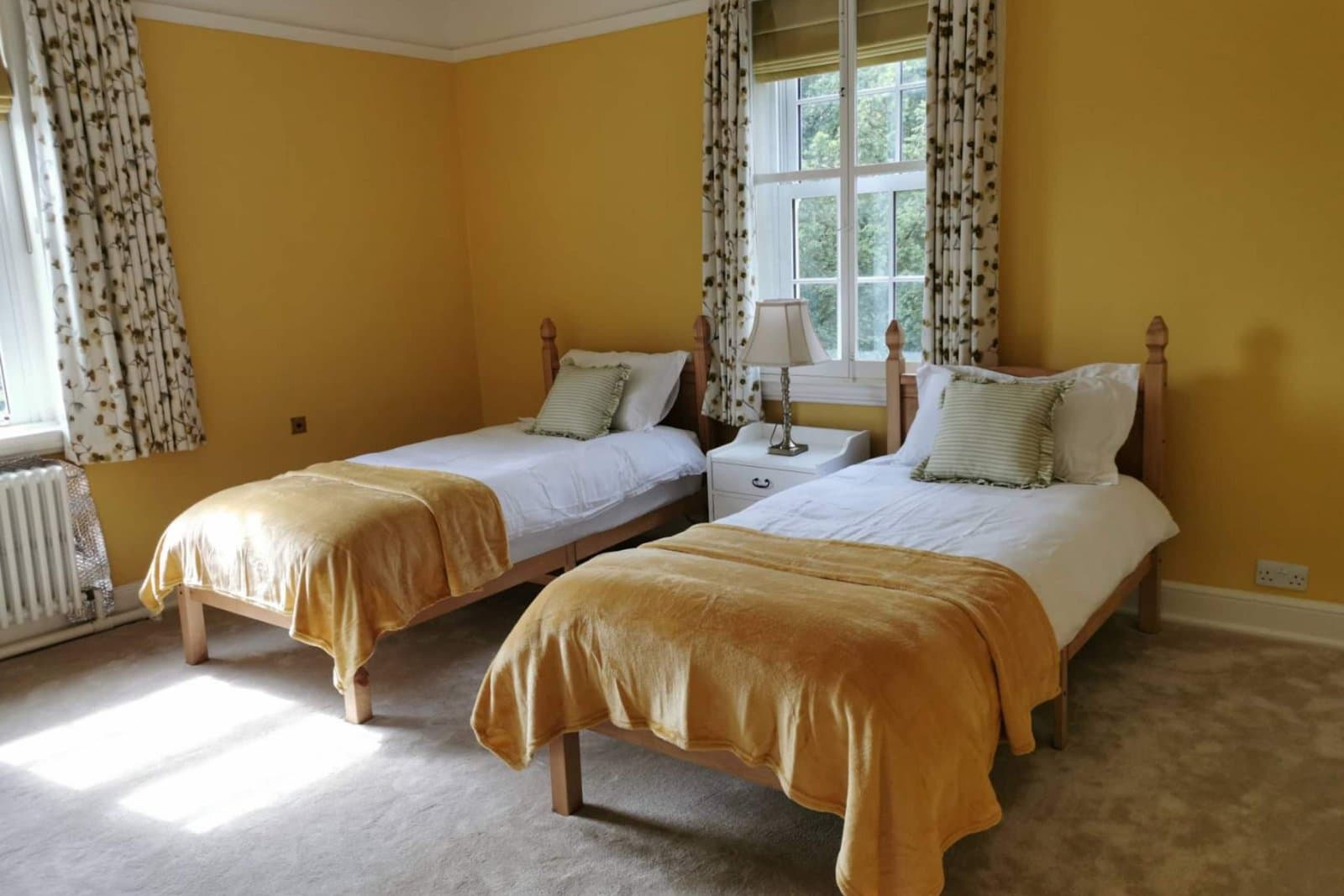 A twin bedroom with ochre walls, two single beds with gold throws and a window onto the grounds