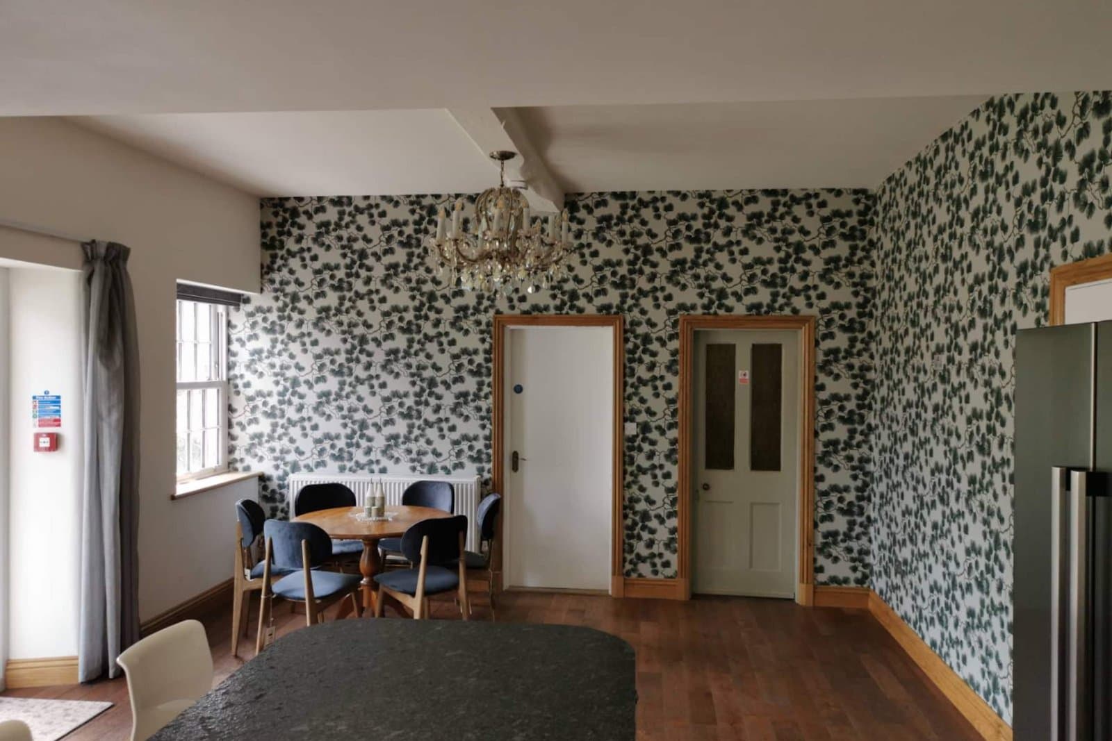 The garden room off the kitchen, with botanical wallpaper, a round breakfast table and a chandelier