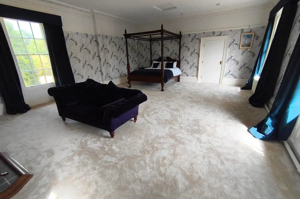 A four-poster bedroom with patterned wallpaper and navy curtains